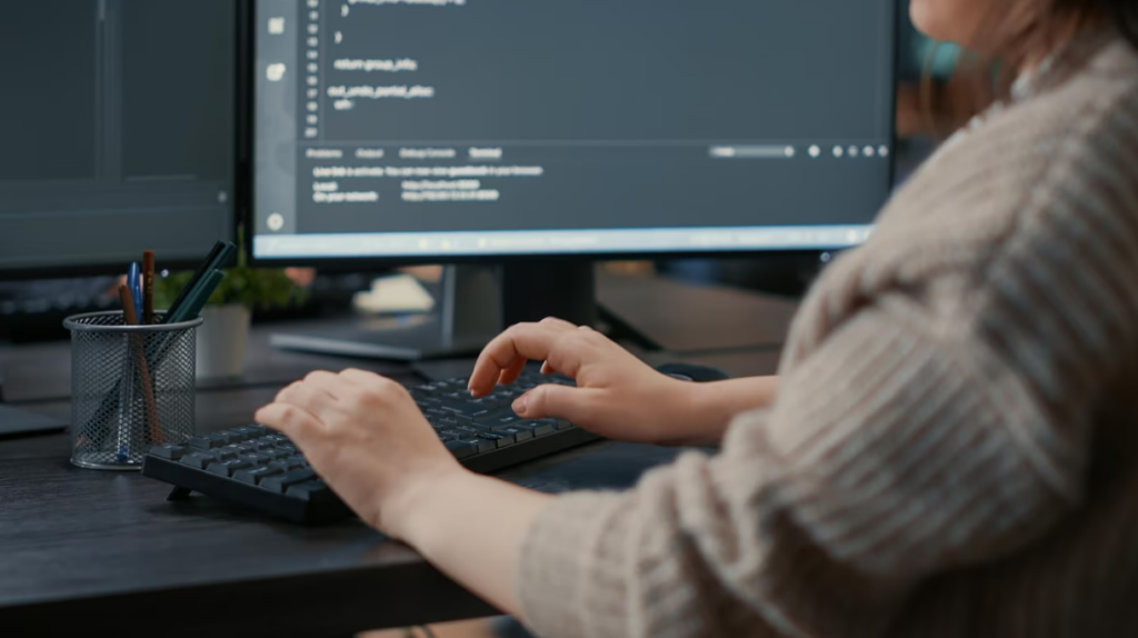 woman in a beige sweater typing on the computer keyboard, coding on computer screen